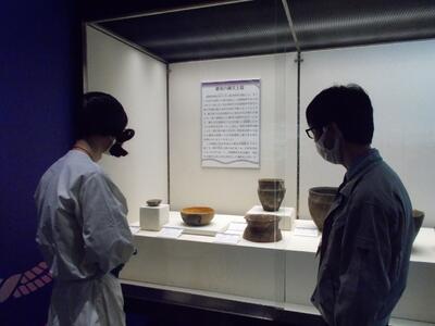 展示ケース「最後の縄文土器」を見る古代人と学芸員。